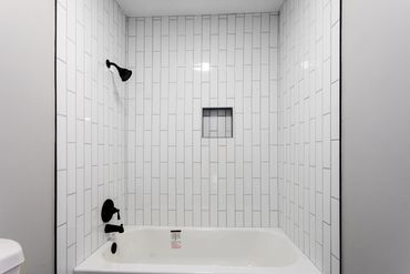 Modern bathtub with white vertical subway tiles and black fixtures.