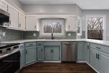 A modern kitchen with green lower cabinets and white upper cabinets.