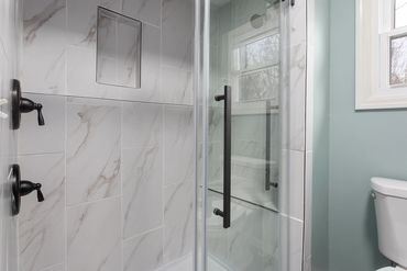 Modern shower with marble tiles and black fixtures next to a toilet.