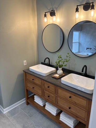 Modern bathroom with wooden vanity, dual sinks, round mirrors, and warm lighting.