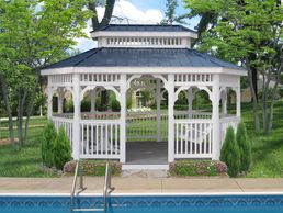 White gazebo with a black roof near a swimming pool in a green garden.