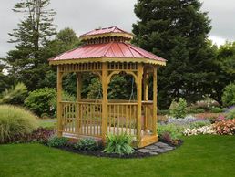Wooden gazebo with red roof in a lush garden.