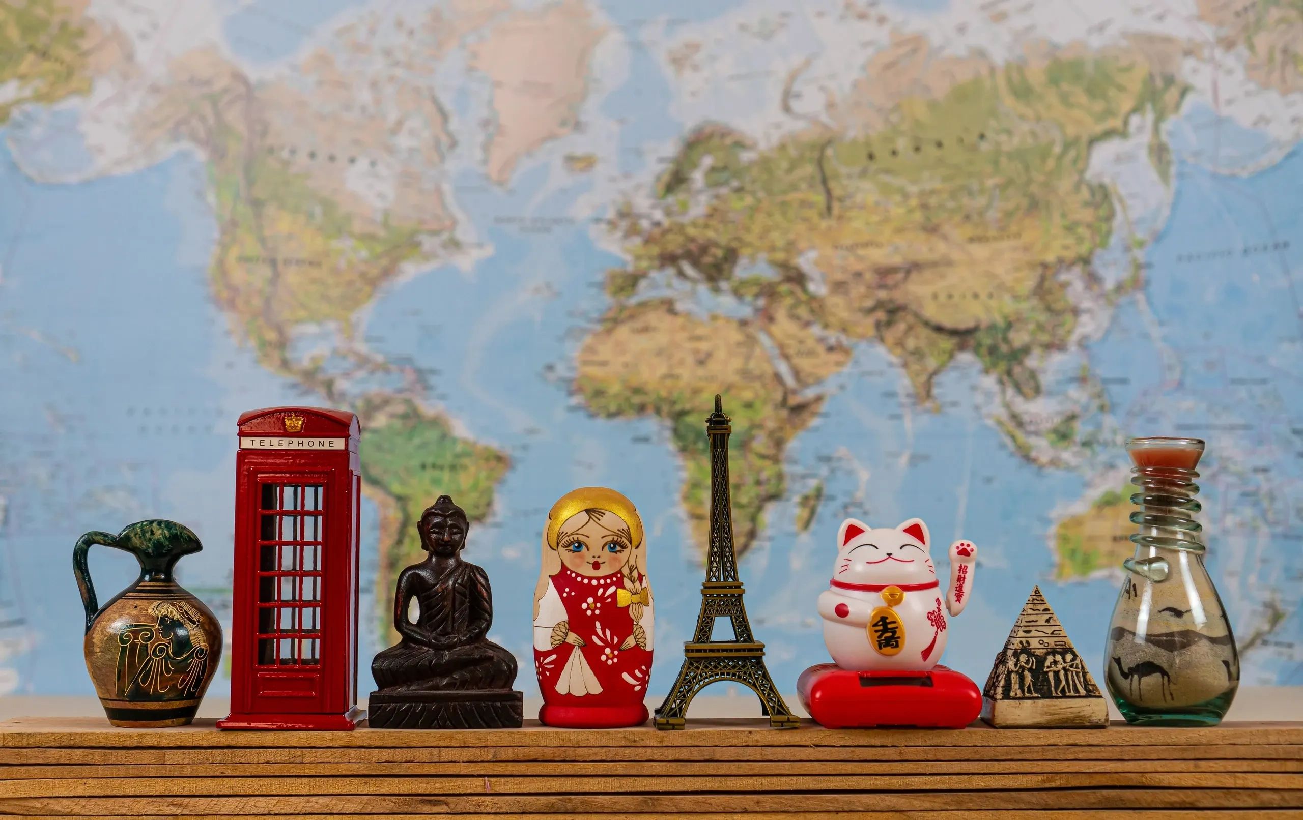 Miniature souvenirs from different countries on a wooden shelf with a world map background.