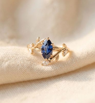 Artistic flat lay photograph of marquise-cut blue sapphire engagement ring with organic leaf and vin