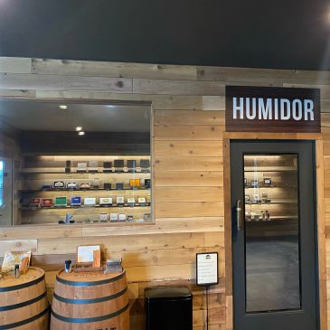 Wood-paneled room with a door labeled HUMIDOR and barrels with display items.