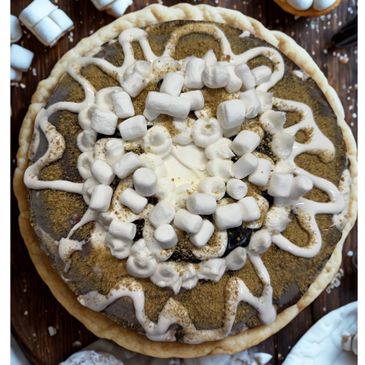 A pie topped with mini marshmallows and drizzled cream on a wooden surface.