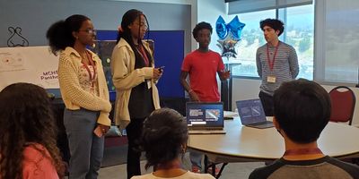 Four young people presenting in a classroom to seated peers.