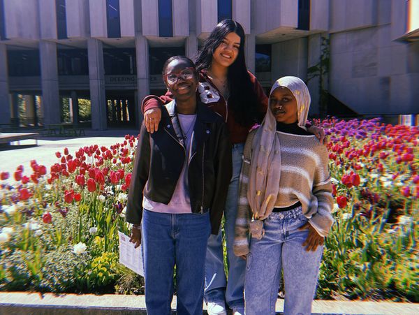 Three friends smiling in front of colorful tulips outside a building.
