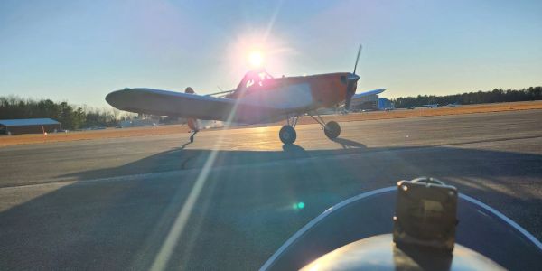 A small propeller airplane on the runway with the sun shining behind it.