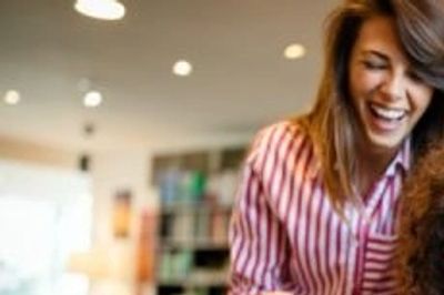 Woman talking to another person laughing. Lights on the ceiling. Books on bookshelves in background