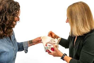 Two women examining a pelvic bone model in a medical or educational setting.