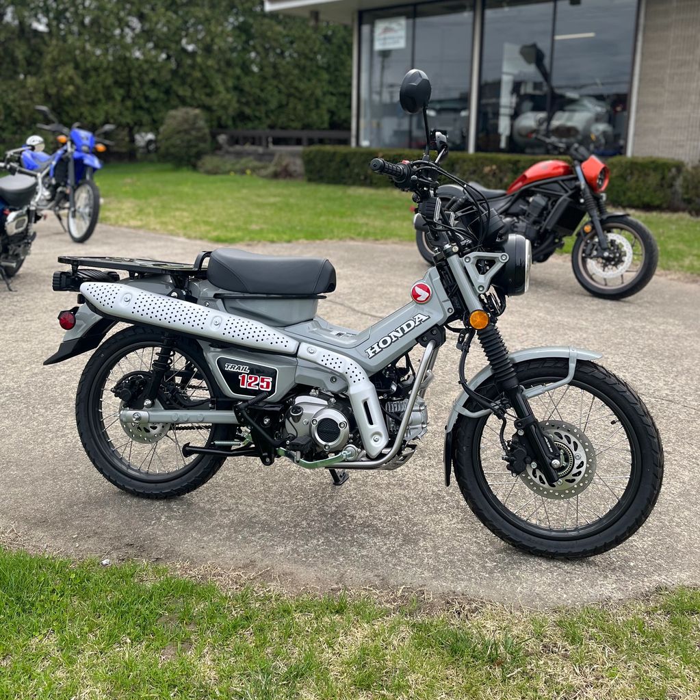 Gray Honda Trail 125 motorcycle parked outside with other bikes in the background.