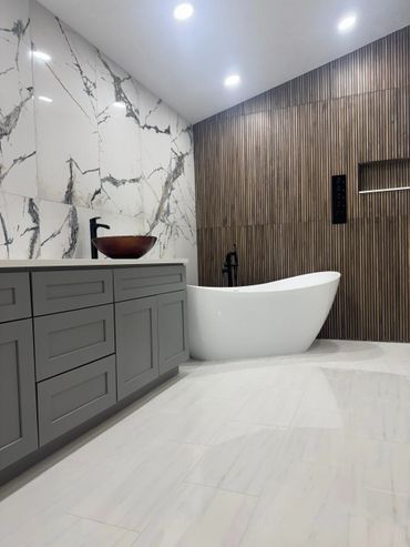 Modern bathroom with marble walls, wooden paneling, and a sleek white bathtub.