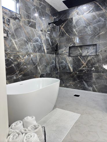 Modern bathroom with a white freestanding tub and dark marble walls.