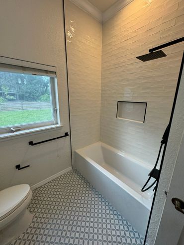 Modern bathroom with white tiles, patterned floor, and black fixtures.