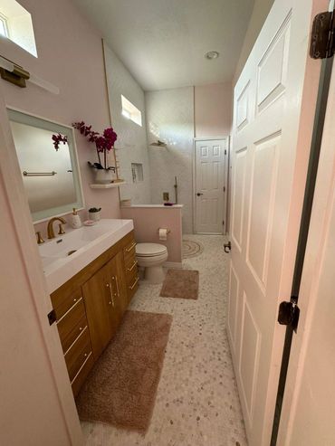 Modern bathroom with wooden vanity, gold fixtures, and pink accents.