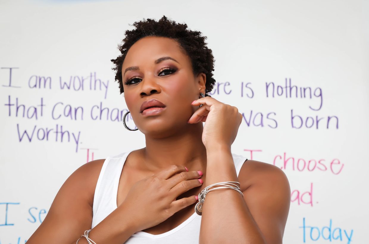 Karla J Noland (African-American woman) standing confidently in front of an affirmation wall.