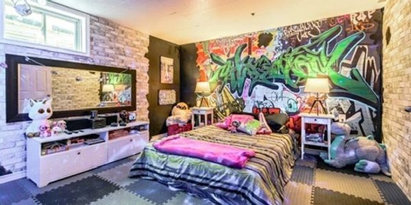 Colorful bedroom with graffiti wall art, stuffed animals, and cozy bedding.