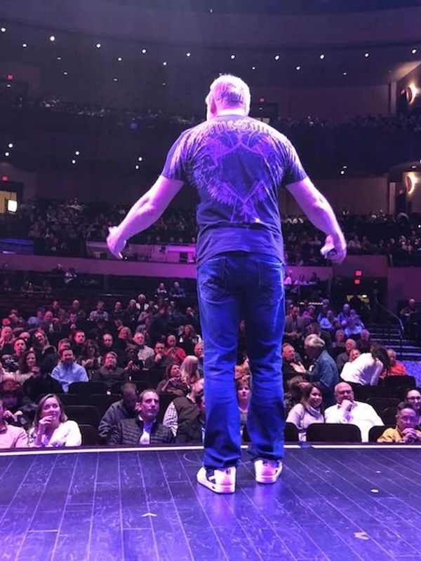 Man speaking on stage to a large audience in an auditorium.