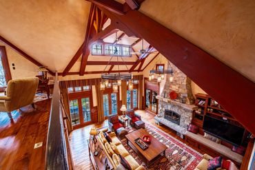 Rustic living room with high ceilings, stone fireplace, and warm wooden beams.