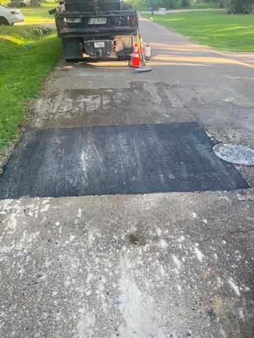 New asphalt patch on a street with a rental truck and traffic cones.