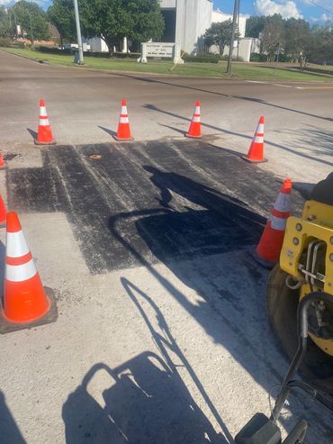 Fresh asphalt patch on a road section with traffic cones.