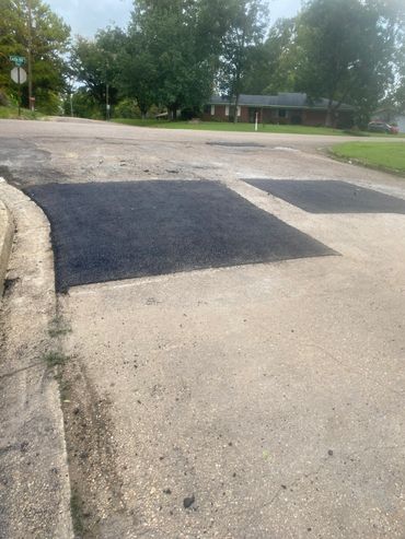 Road with fresh asphalt patches in a residential neighborhood.