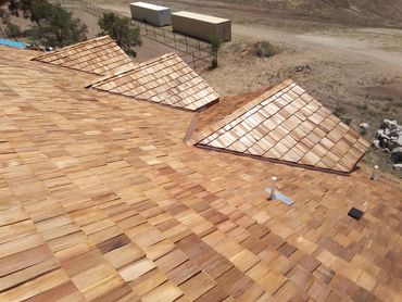 Newly installed wooden shingle roof on a rural building under clear sunlight.
