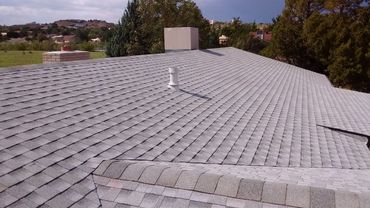 Gray shingle roof with vents and chimney in a suburban neighborhood.