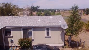 Rural house with gray roof, satellite dish, and surrounding trees under a clear sky.