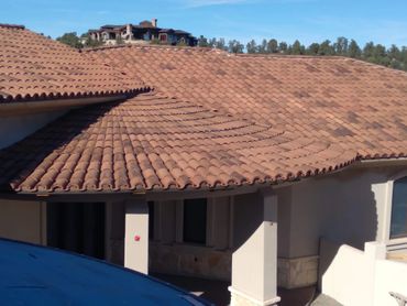 Terracotta tiled roof with a mountainous house background under a clear blue sky.