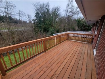 Spacious wooden balcony overlooking a green backyard with trees.