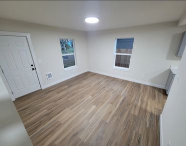 Empty room with wood flooring, white walls, and two windows under bright ceiling light.