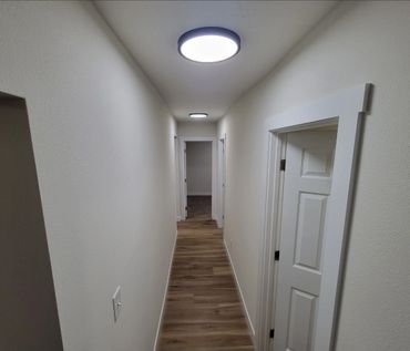 A narrow hallway with wooden flooring and white walls, illuminated by modern ceiling lights.