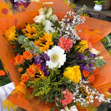 Vibrant mixed flower bouquet wrapped in orange paper.