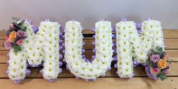 Floral arrangement spelling 'MUM' with white flowers and colorful roses.