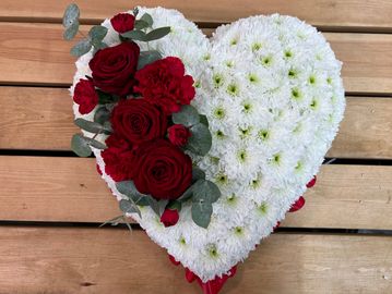 Heart-shaped floral arrangement with white and red flowers on a wooden surface.