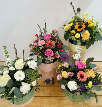 Four colorful floral arrangements in pastel round boxes on a wooden surface.