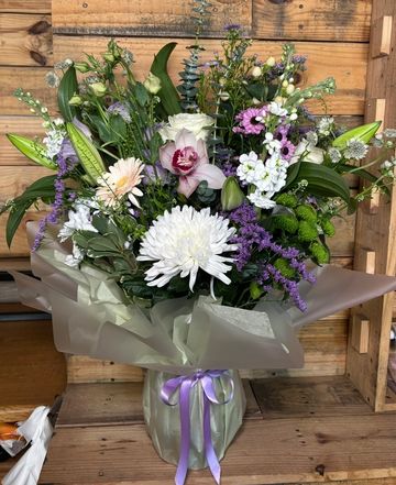 Elegant mixed flower bouquet with white, purple, and green blooms wrapped in soft lavender paper.