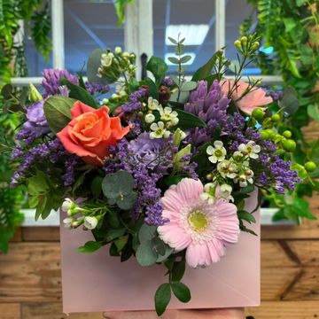 A vibrant mixed bouquet with roses, daisies, and lavender in a pink box.