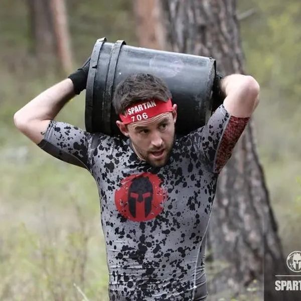 Man in a Spartan race carrying a heavy bucket on his shoulders.