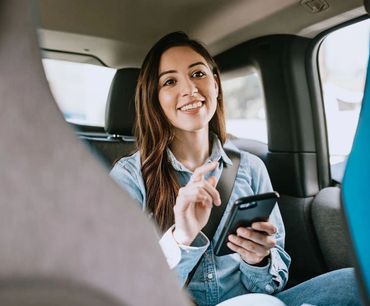A smiling woman using her smartphone in the backseat of a car.