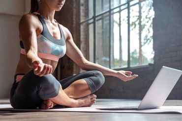 A woman doing yoga in front of her laptop