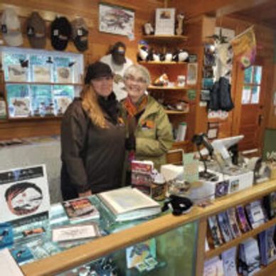 Two women smiling behind a store counter filled with books and merchandise.