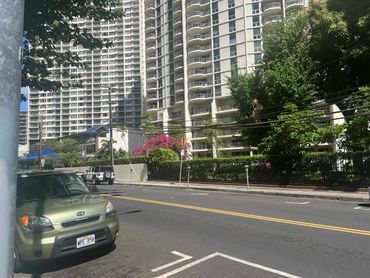 Street view with parked cars and tall residential buildings under a sunny sky.