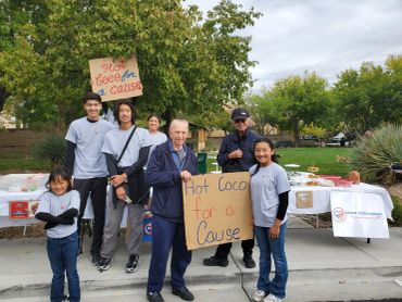 Group of people holding signs promoting hot cocoa for a cause outdoors.