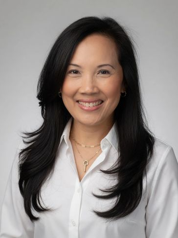 Smiling woman with long black hair in a white shirt against a gray background.