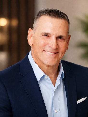 Smiling man in a navy blue blazer and light blue shirt posing indoors.