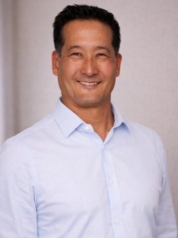 Smiling man in a light blue shirt posing against a neutral background.