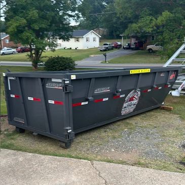 Large black dumpster on a residential lawn.